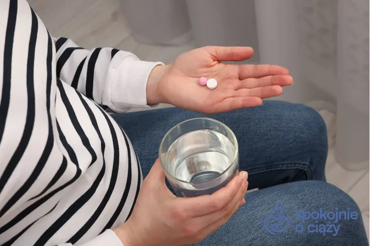 Kobieta w zaawansowanej ciąży ze szklanką wody przyjmująca leki oraz informacje, czy apap w ciąży jest bezpieczny
