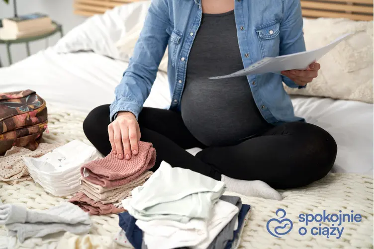 Kobieta w zaawansowanej ciąży siedząca z listą i ubrankami na podłodze, a także wyprawka do szpitala krok po kroku