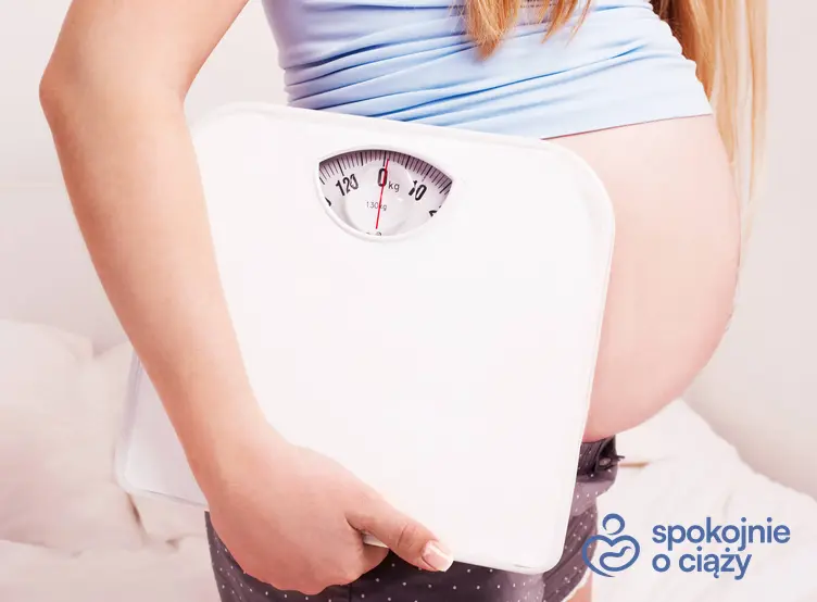 Kobieta w zaawansowanej ciąży trzymająca wagę pod pachą, a także prawidłowe BMI w ciąży