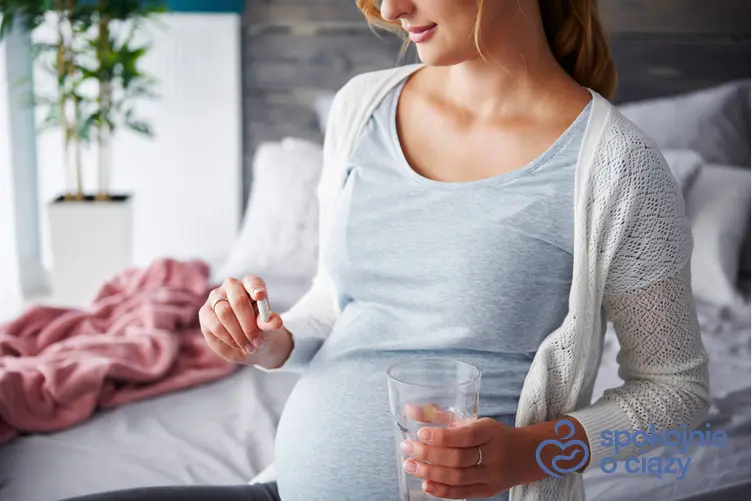 Kobieta w zaawansowanej ciąży trzymająca szklankę i tabletkę, a także kwas foliowy w ciąży krok po kroku