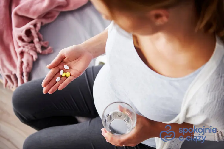Kobieta w zaawansowanej ciąży trzymająca szklankę z wodą i tabletki, a także witaminy w ciąży krok po kroku