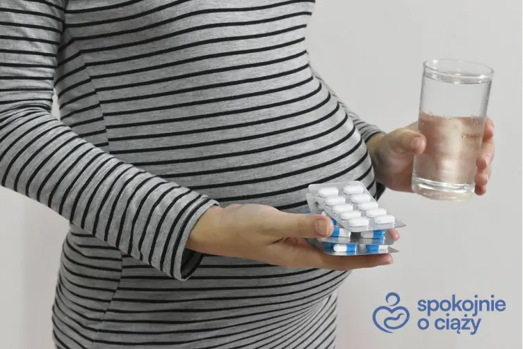 Kobieta w zaawansowanej ciąży trzymająca szklankę z wodą i tabletki, a także witaminy w ciąży bez tajemnic