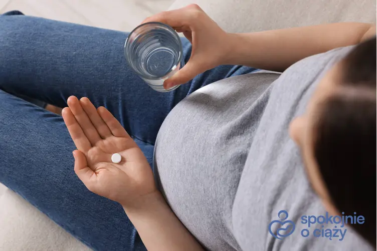 Kobieta w zaawansowanej ciąży trzymająca szklankę i tabletkę, a także wapń w ciąży
