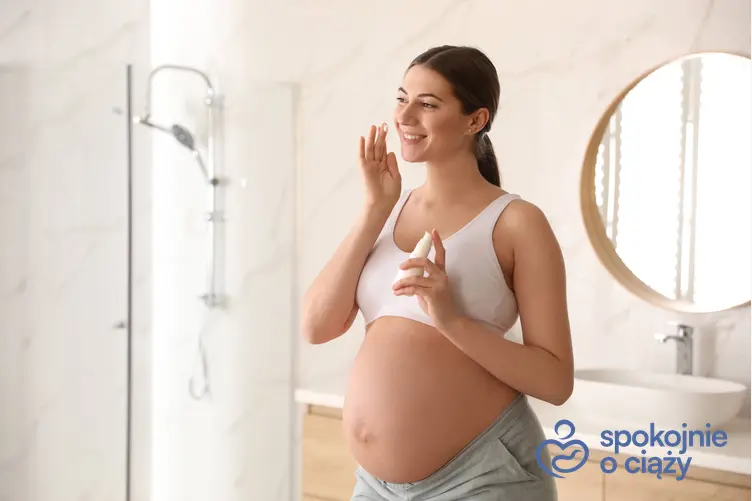 Kobieta w zaawansowanej ciąży nakładająca krem na twarz, a także kosmetyki dla kobiet w ciąży