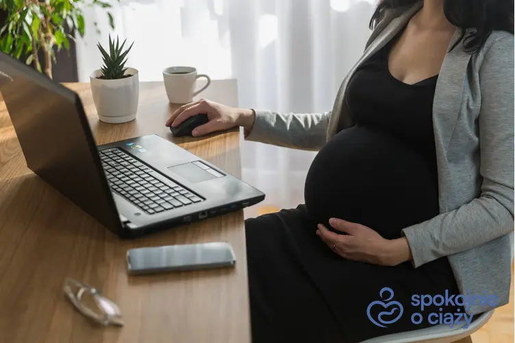 Kobieta w zaawansowanej ciąży siedząca w pracy za biurkiem, a także umowa na czas określony a ciąża