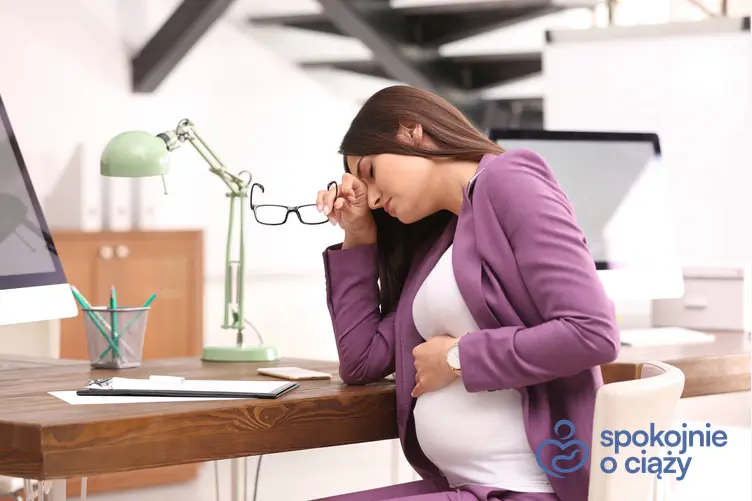 Kobieta w zaawansowanej ciąży zmęczona za biurkiem w pracy, a także zwolnienie lekarskie w ciąży