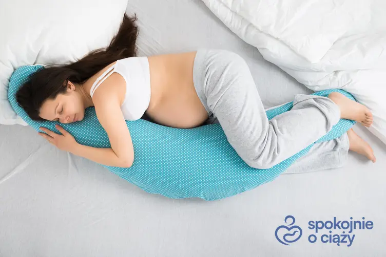 Kobieta w ciąży śpiąca na łóżku na poduszce typu rogal, a także rogal do spania w ciąży bez tajemnic