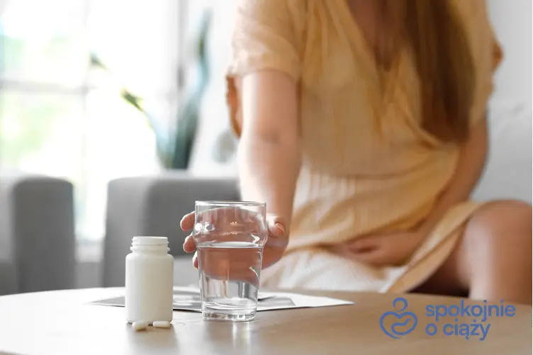Kobieta w zaawansowanej ciąży siegająca po szklankę wody i lek, a także porady, czy Acard w ciąży jest bezpieczny