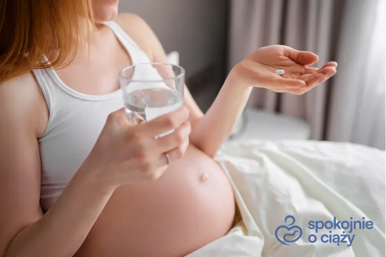Kobieta w zaawansowanej ciąży trzymająca tabletkę i wodę, a także czy Acard w ciąży jest bezpieczny