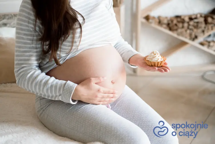 Kobieta w zaawansowanej ciąży trzymająca na dłoni babeczkę, a także insulinooporność w ciąży