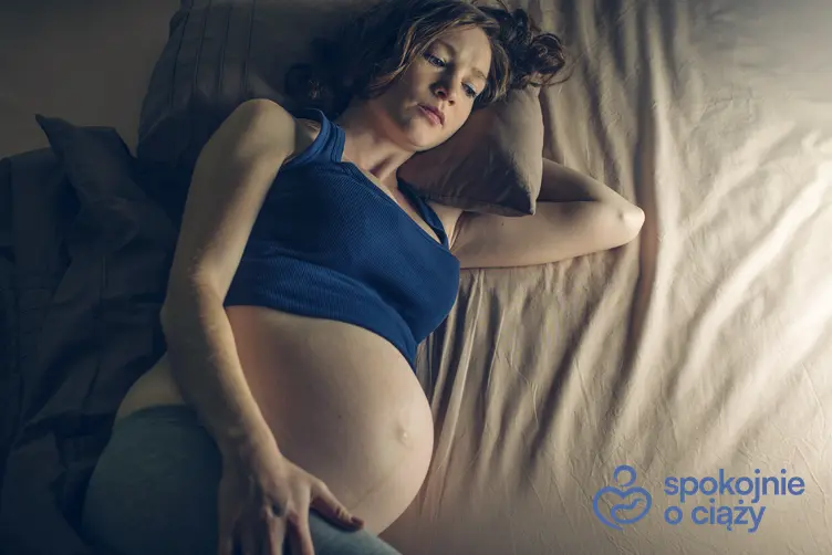 Kobieta w zaawansowanej ciąży leżąca na łóżku, a także czy brak snu w ciąży szkodzi dziecku