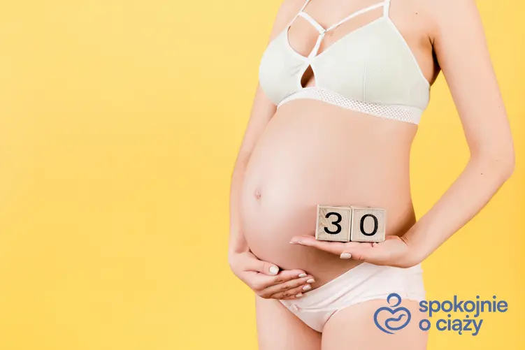 Kobieta w zaawansowanej ciąży trzymająca się za brzuch, a także 30 tydzień ciąży krok po kroku