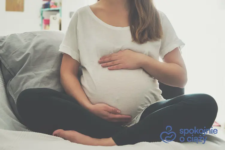 Kobieta w zaawansowanej ciąży trzymająca się za brzuch, a także 32 tydzień ciąży krok po kroku