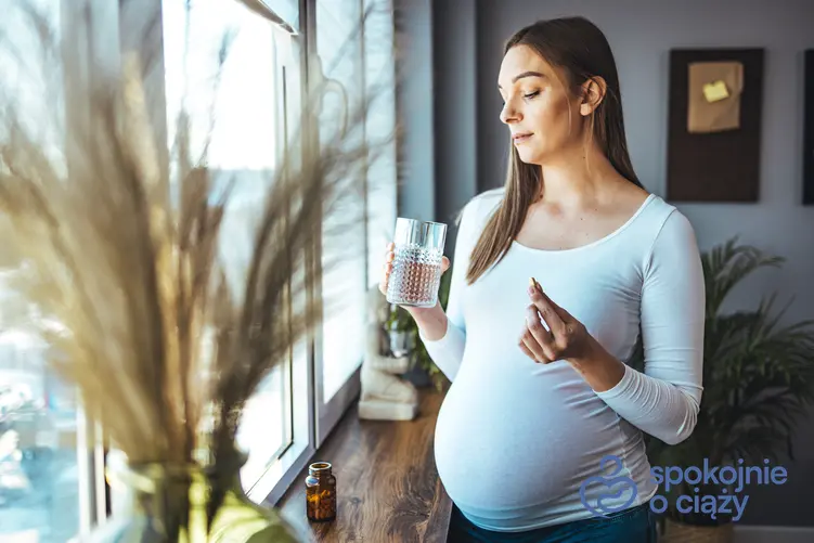 Kobieta w zaawansowanej ciąży trzymająca lek i szklankę z wodą oraz wzdęcia w ciąży