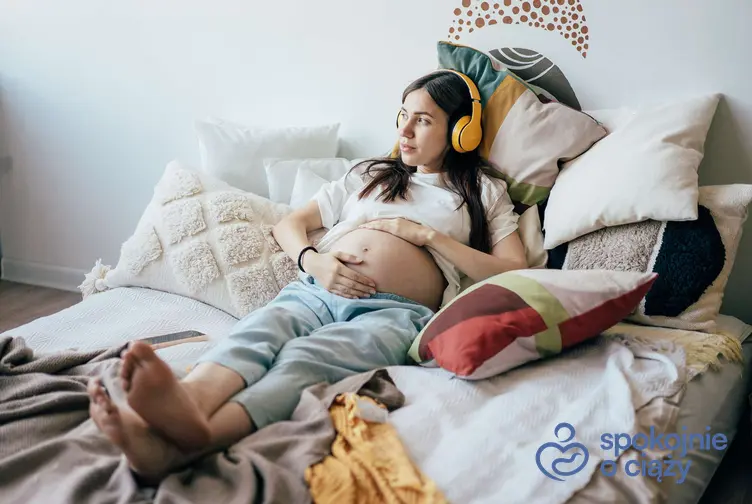 Kobieta w ciąży leży na łóżku i słucha muzyki