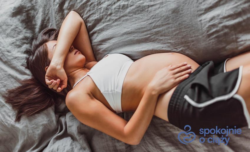Kobieta w zaawansowanej ciąży leżąca na łóżku, a także mdłości w ciąży i sposoby na nie