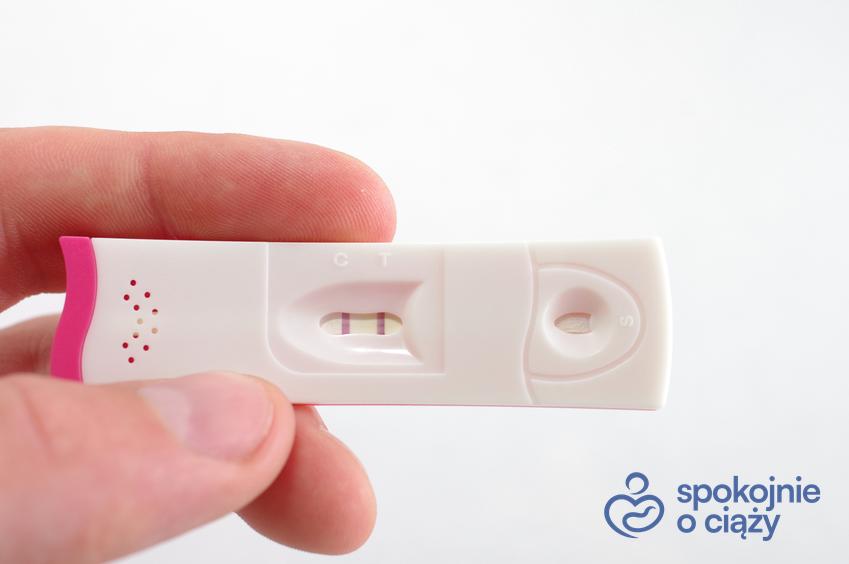 Test ciążowy pozytywny trzymany w dłoni na białym tle, a także porady położnej, jak zajść w ciążę