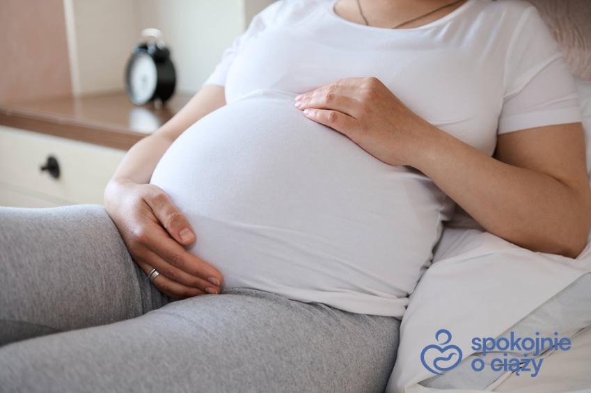 Kobieta w zaawansowanej ciąży oparta na łóżku, a także jaka poduszka do spania w ciąży sprawdzi się najlepiej