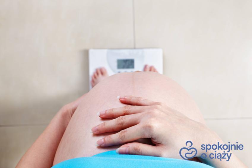 Kobieta w zaawansowanej ciąży stojąca na wadze z odsłoniętym brzuchem oraz jakie powinno być BMI w ciąży