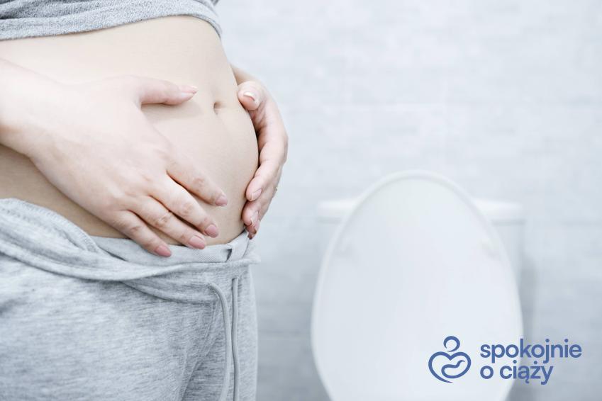 Kobieta w zaawansowanej ciąży trzymająca się za brzuch w toalecie, a także zaparcia w ciąży