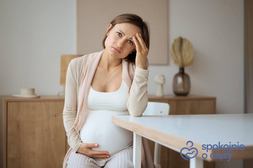Kobieta w zaawansowanej ciąży siedząca i trzymająca się za głowę, a także ból głowy w ciąży