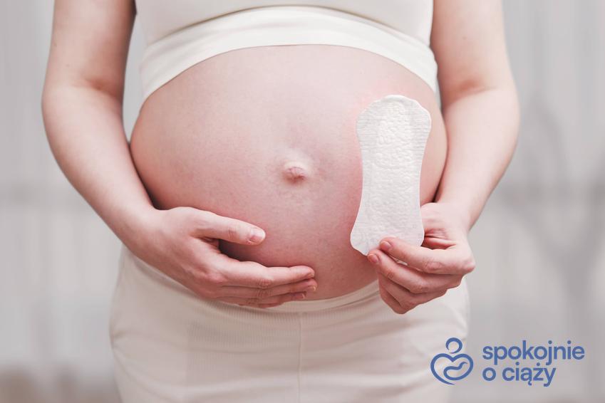 Kobieta w zaawansowanej ciąży trzymająca wkładkę higieniczną, a także okres w ciąży
