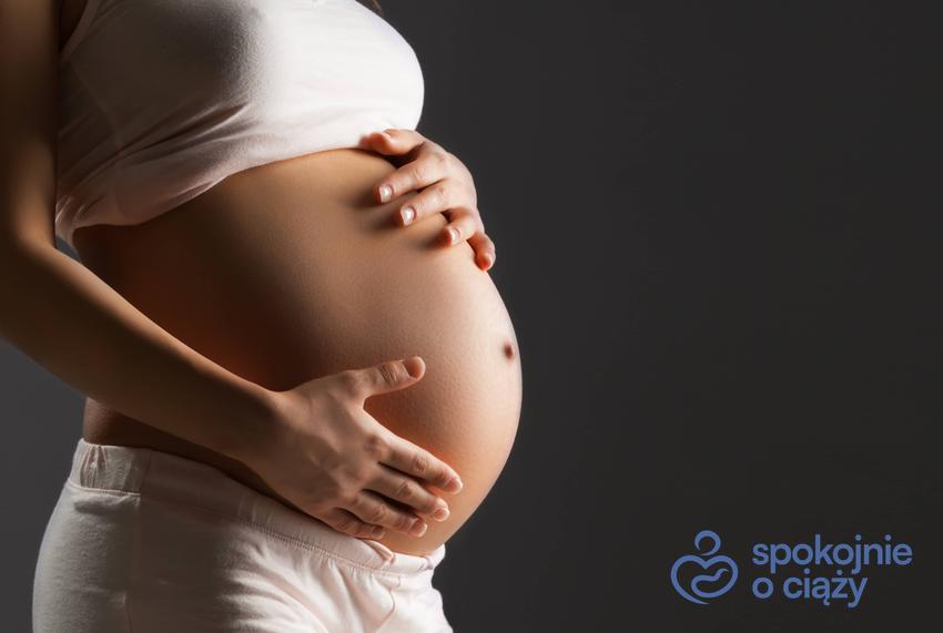 Kobieta w zaawansowanej ciąży trzymająca się za brzuch na czarnym tle, a także twardy brzuch w ciąży bez tajemnic