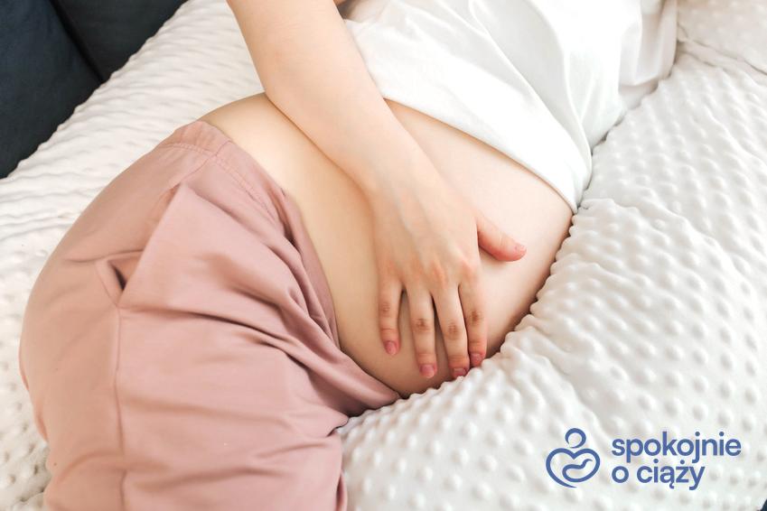 Kobieta w zaawansowanej ciąży leżąca na łóżku i trzymająca się za brzuch, a także ból żołądka w ciąży bez tajemnic