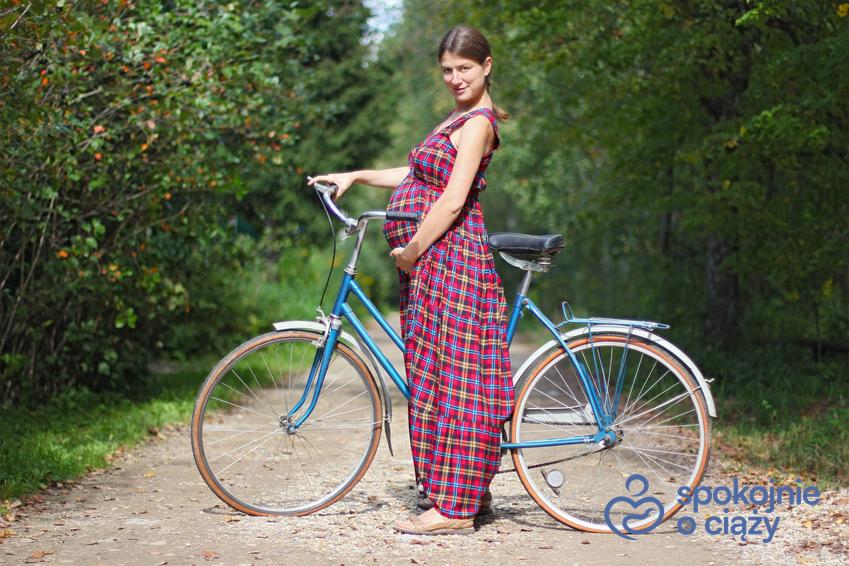 Kobieta w zaawansowanej ciąży stojąca przy rowerze, a także informacje, czy w ciąży można jeździć na rowerze