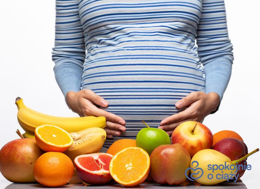 Kobieta w ciąży przed blatem pełnym owoców, a także zakazane owoce i warzywa w ciąży