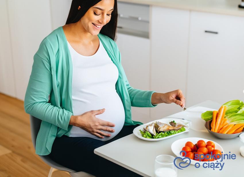 Kobieta w ciąży siedząca przy stole i jedząca ryby, a także DHA w ciąży bez tajemnic