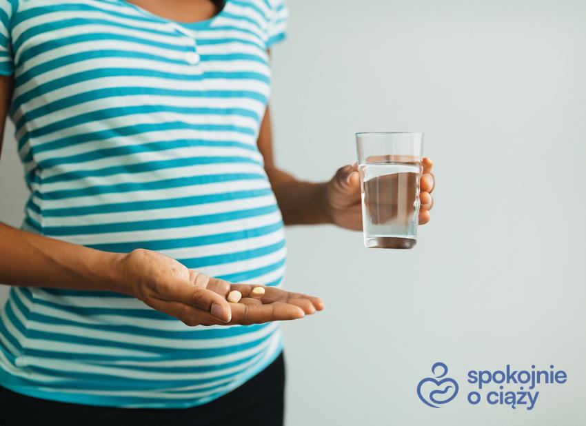 Kobieta w ciąży trzymająca tabletkę i szklankę wody, a także DHA w ciąży krok po kroku