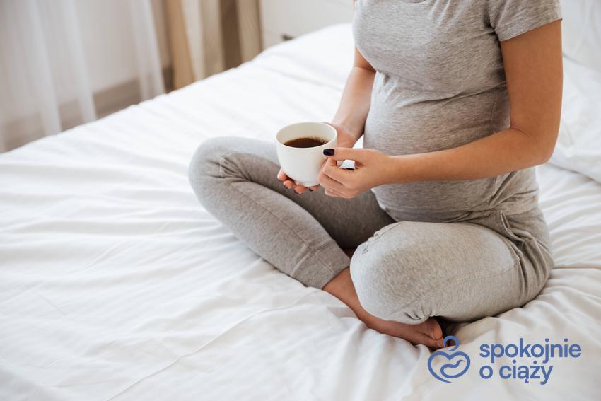 Kobieta w zaawansowanej ciąży siedząca na łóżku z kubkiem herbaty, a także czy czarna herbata w ciąży jest bezpieczna