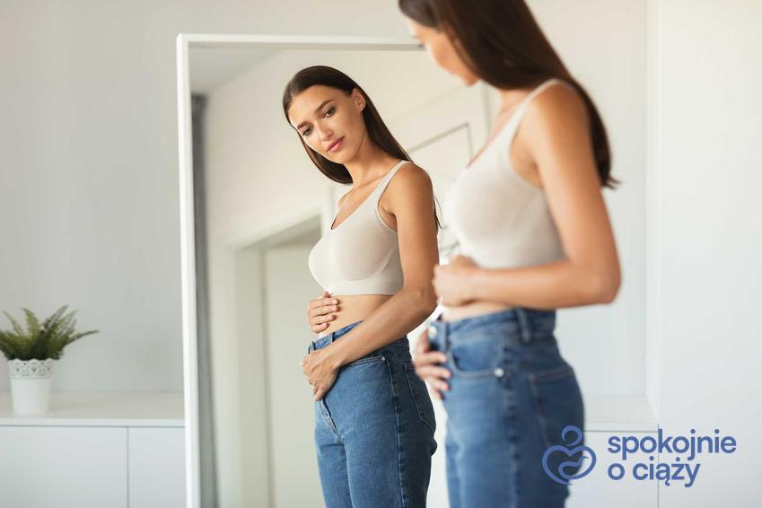 Kobieta oglądająca się w lustrze, a także 1 miesiąc ciąży i jego przebieg, dolegliwości i zalecenia